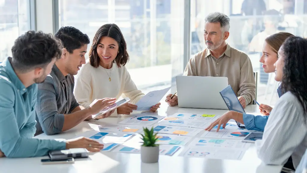 Réunion d'équipe commerciale dans un bureau moderne, discutant de graphiques et de rapports financiers lors d'une session de planification collaborative.